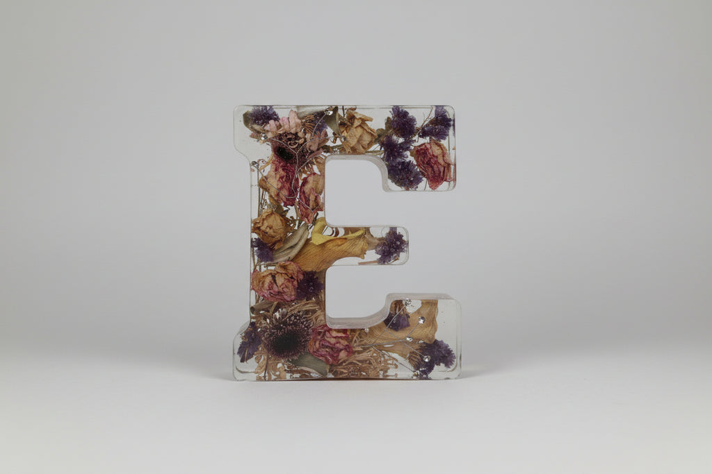 Decorative letters with pressed flowers held by a hand on a white background