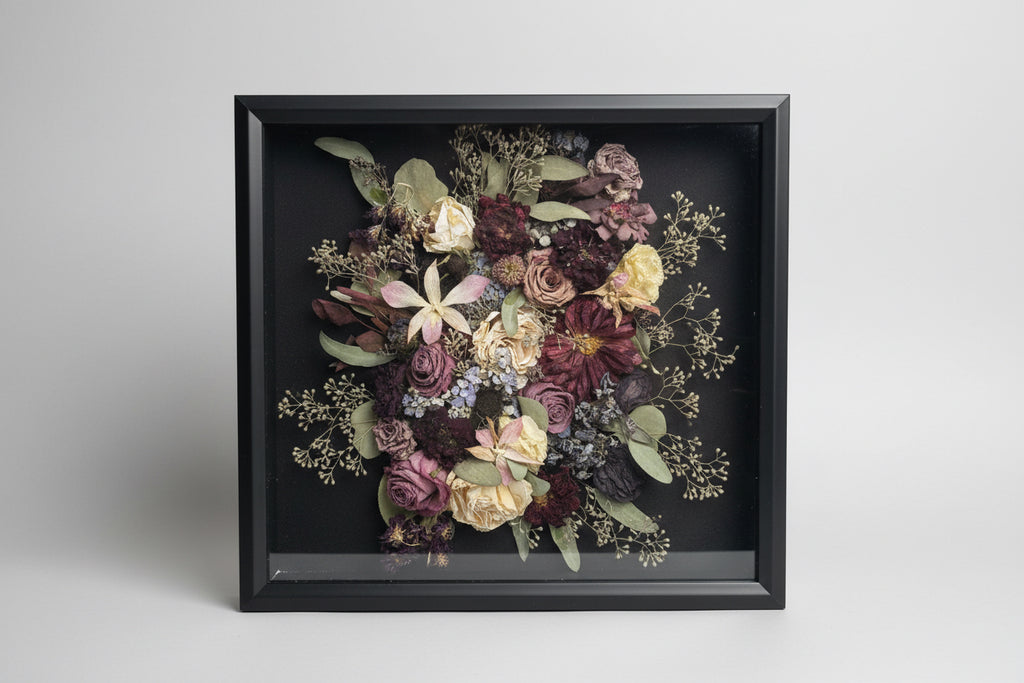 Framed bouquet of dried flowers held by a person against a white brick wall.
