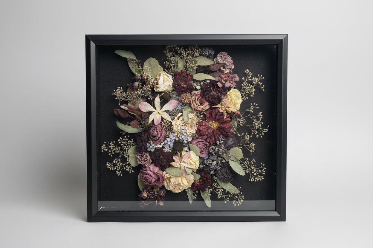 Framed bouquet of dried flowers held by a person against a white brick wall.