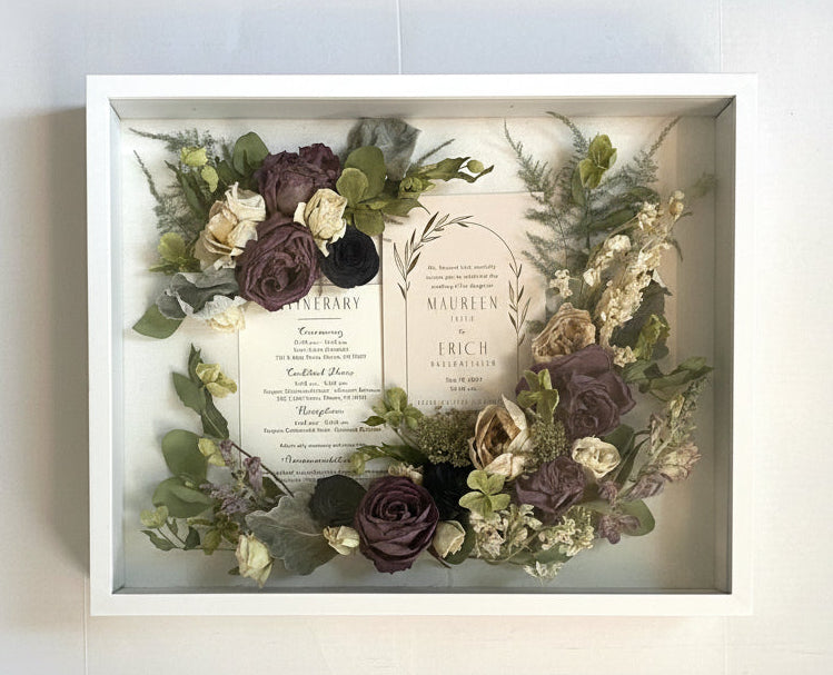 Decorative wreath with flowers and a card inside a framed display on a white background