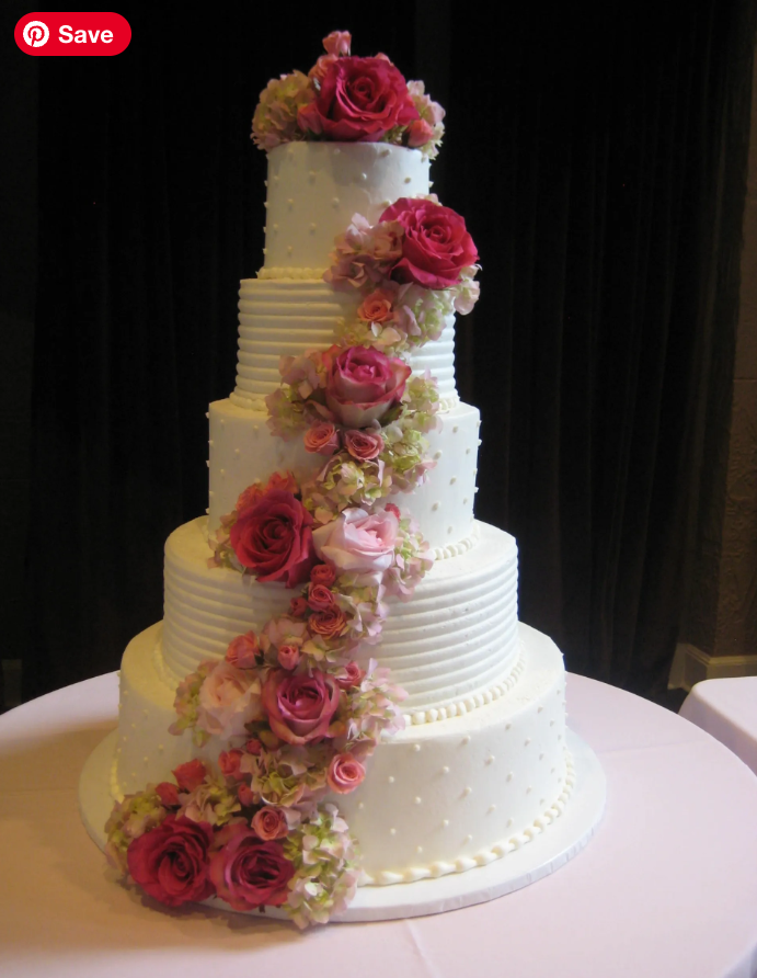A multi-tiered white wedding cake decorated with pink and red floral arrangements