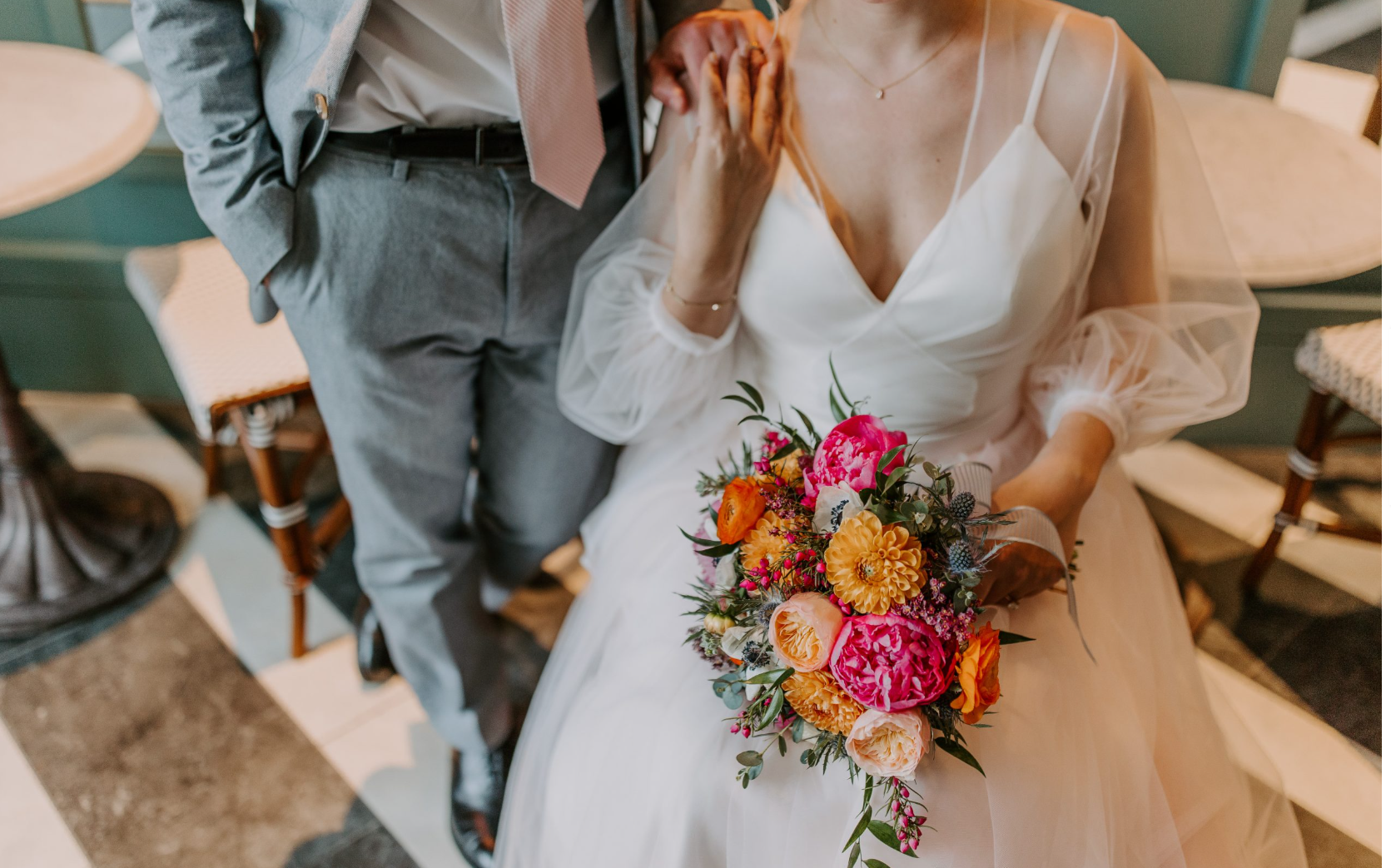  wedding photo showing a bride in a white dress holding a colorful bouquet next to a groom in gray clothing.