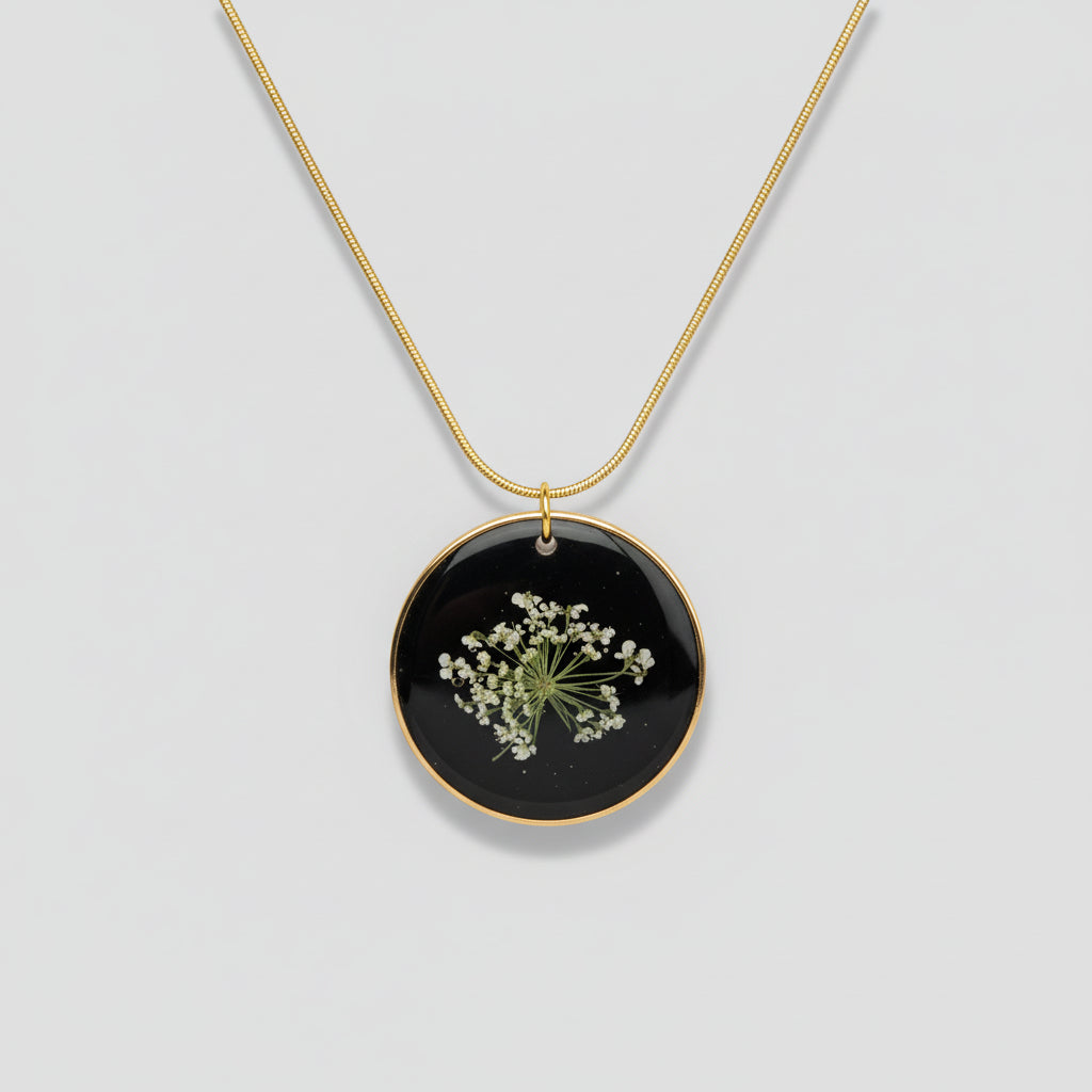 Necklace with a black pendant featuring pressed flowers on a light gray surface