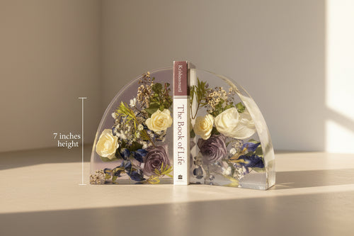 Decorative bookends with floral design and 'Book of Life' book in the center against a white brick wall.