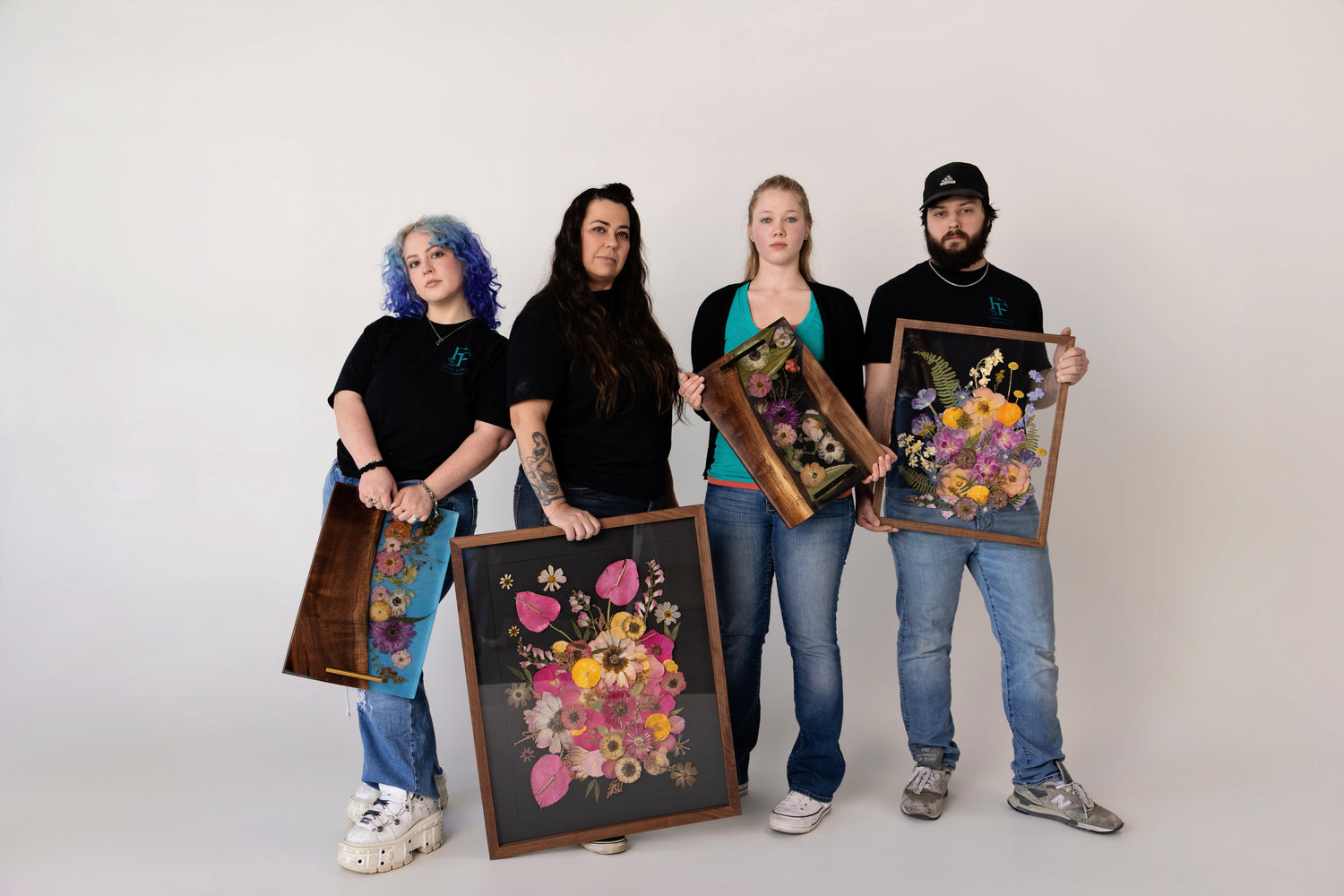 Four people holding floral art pieces against a white background