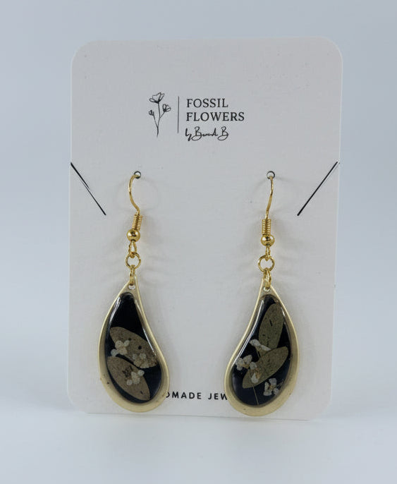 Teardrop-shaped earrings on a Fossil branded card with a wooden surface background
