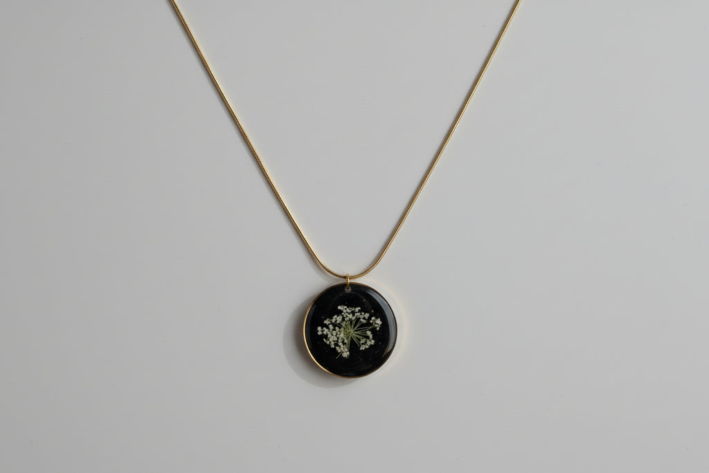 Necklace with a round pendant featuring a pressed flower on a dark background