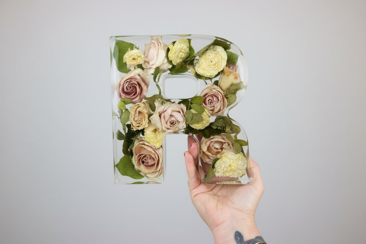 Clear acrylic letter 'R'  filled with preserved flowers on a grey surface.