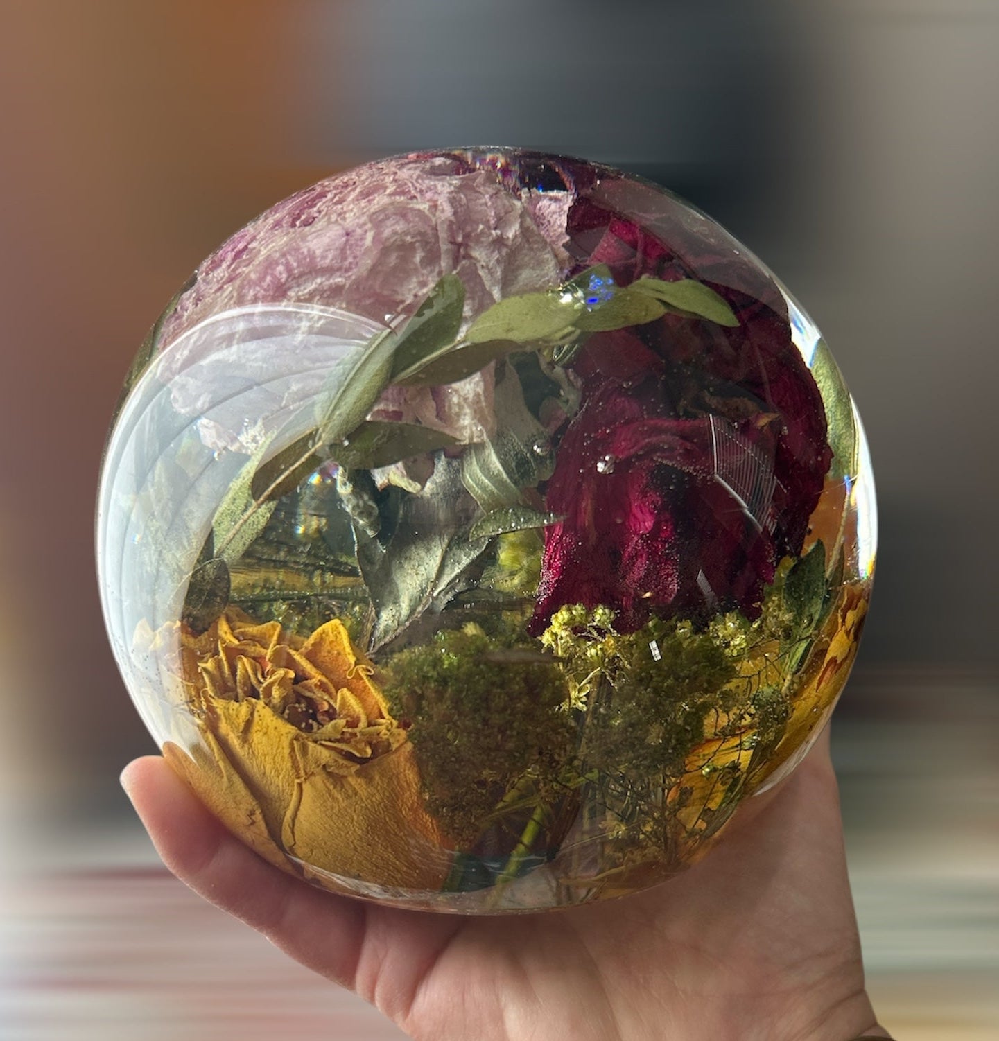 Hand holding a crystal ball filled with dried flowers against a blurred background