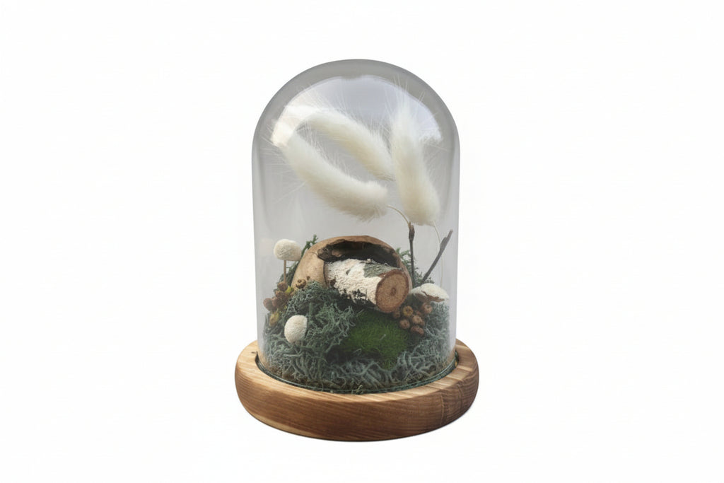 Glass container with a wooden lid, containing a small plant and decorative elements, held by a hand.