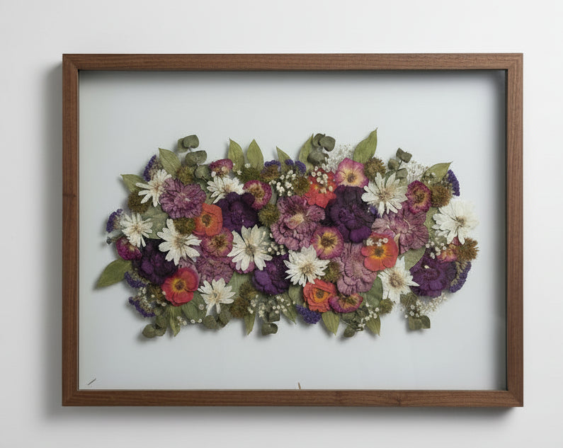 Framed arrangement of pressed flowers on a textured white wall