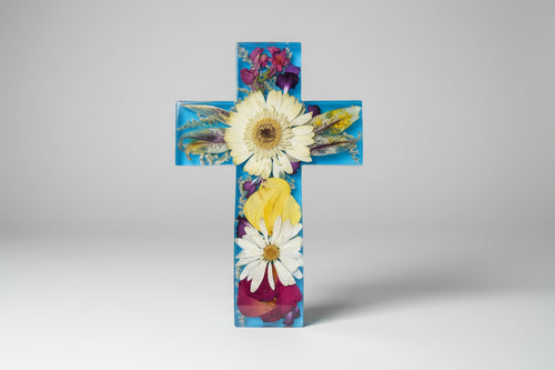 Decorative cross with pressed flowers held by a hand against a grassy background