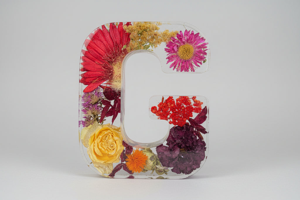 Clear resin letter 'G' with embedded colorful flowers held against a dark background