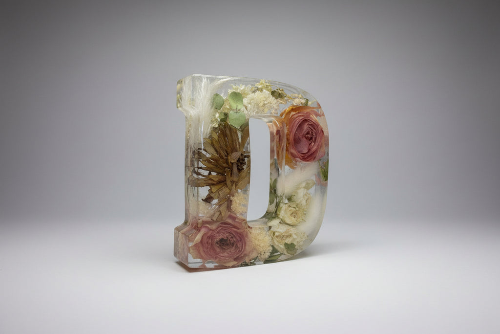 Decorative letter D made of clear resin with preserved flowers flowers on a gray surface.