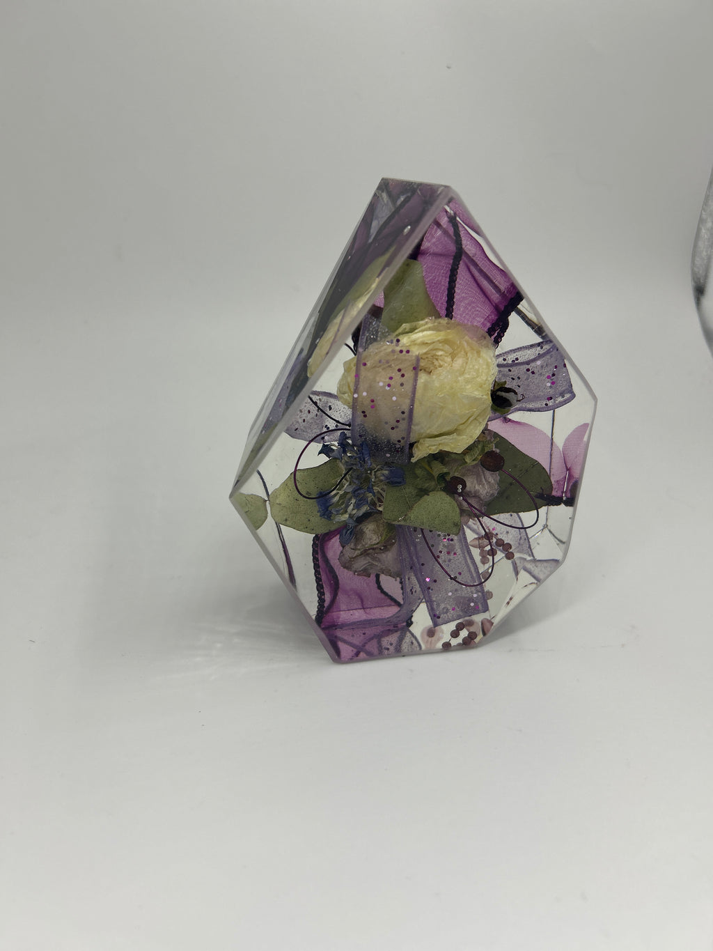 Gemstone resin shape with a white flower corsage with purple ribbon inside
