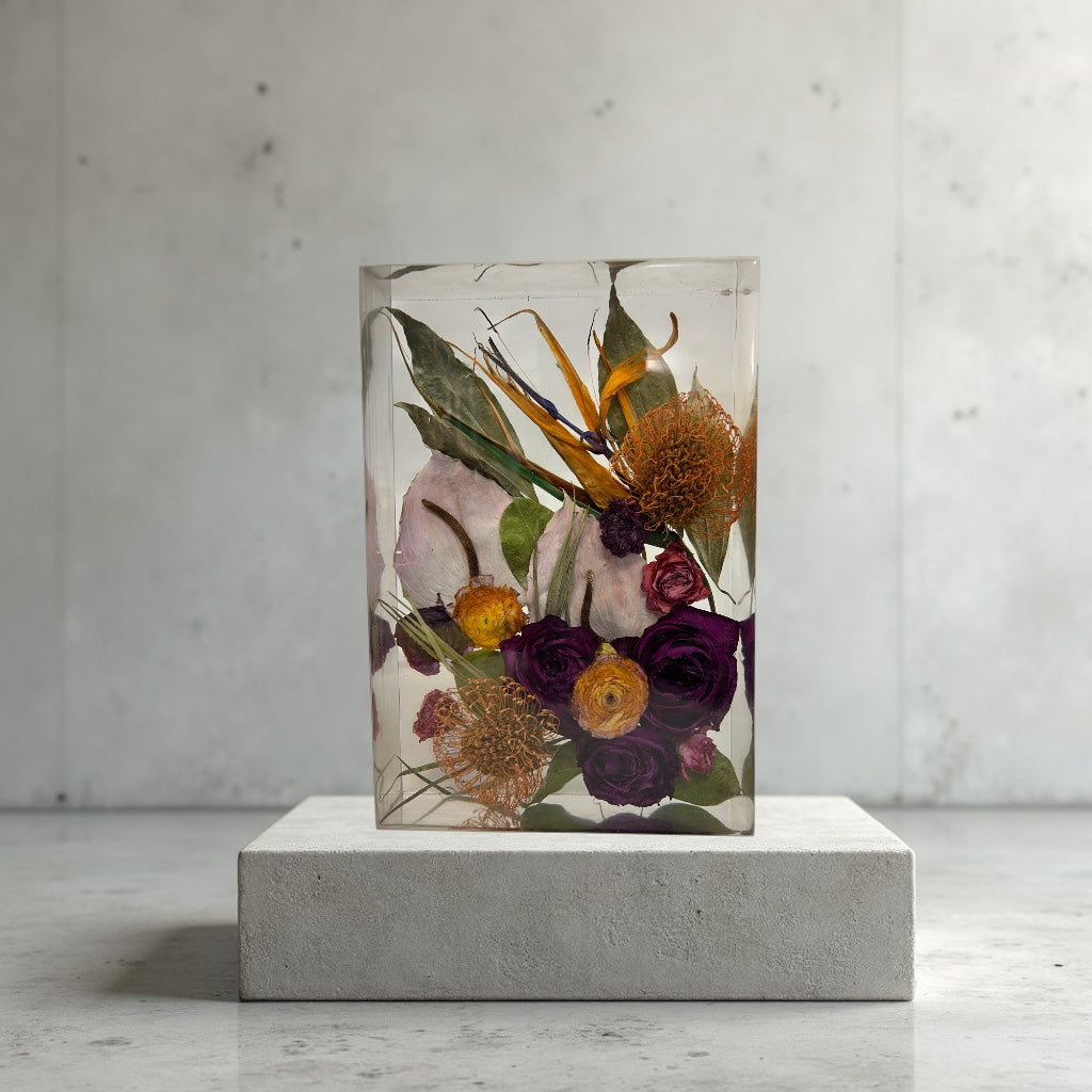 Rectangular resin floral block preserved with purple and orange flowers on a concrete pedestal against a light gray background
