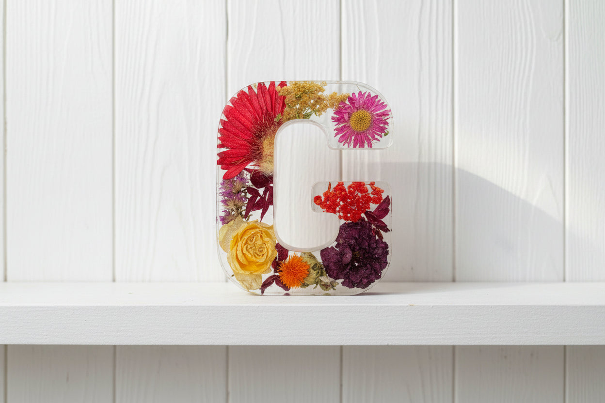 Clear resin letter 'G' with embedded colorful flowers held against a dark background