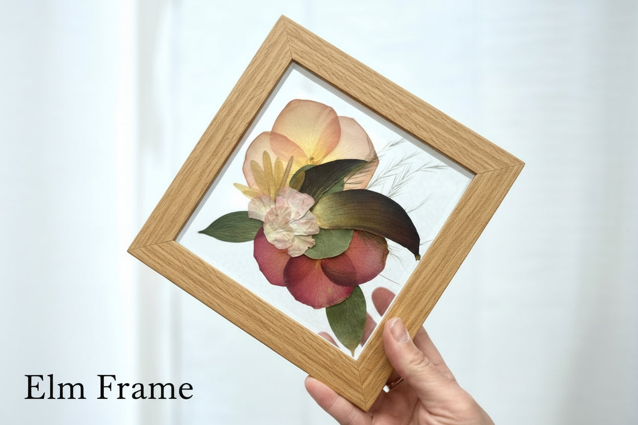 Hand holding a framed floral arrangement with 'Elm Frame' text on a white background