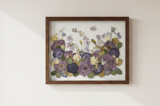 Framed artwork of pressed flowers with a wooden frame on a white wall.