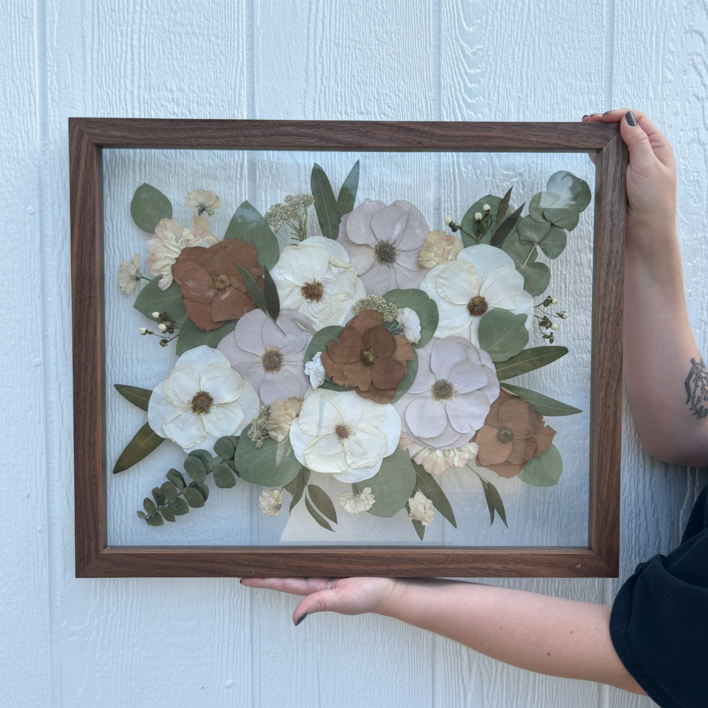 Framed pressed flower arrangement held by a person on a light background
