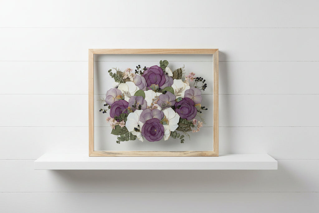 Framed arrangement of pressed flowers with purple and white blossoms on a grey studio