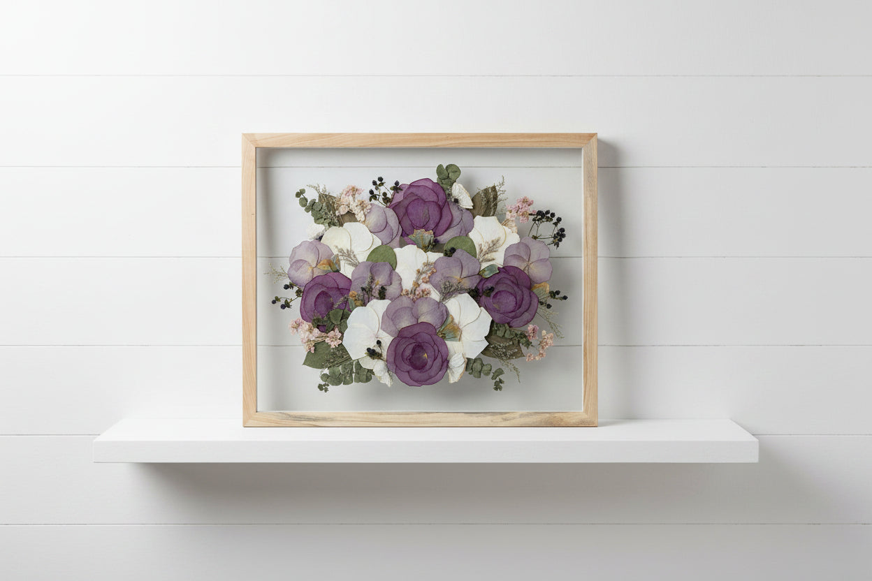 Framed arrangement of pressed flowers with purple and white blossoms on a grey studio