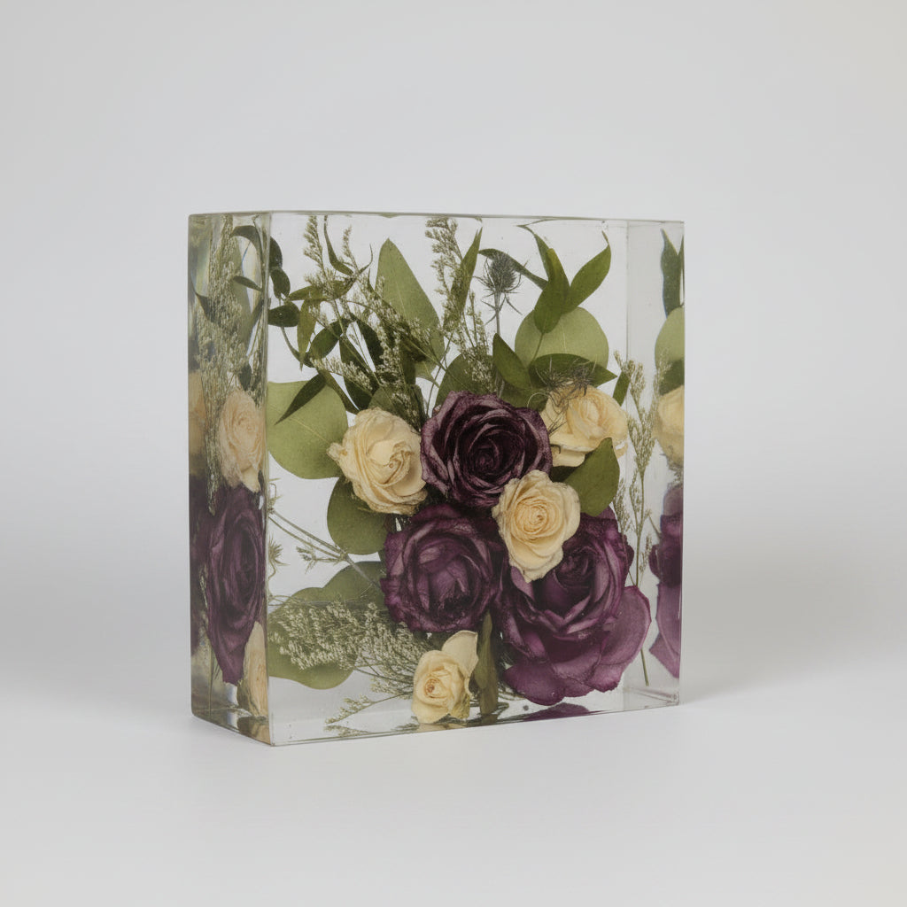 Square glass block with preserved flowers including purple and yellow roses on a white background