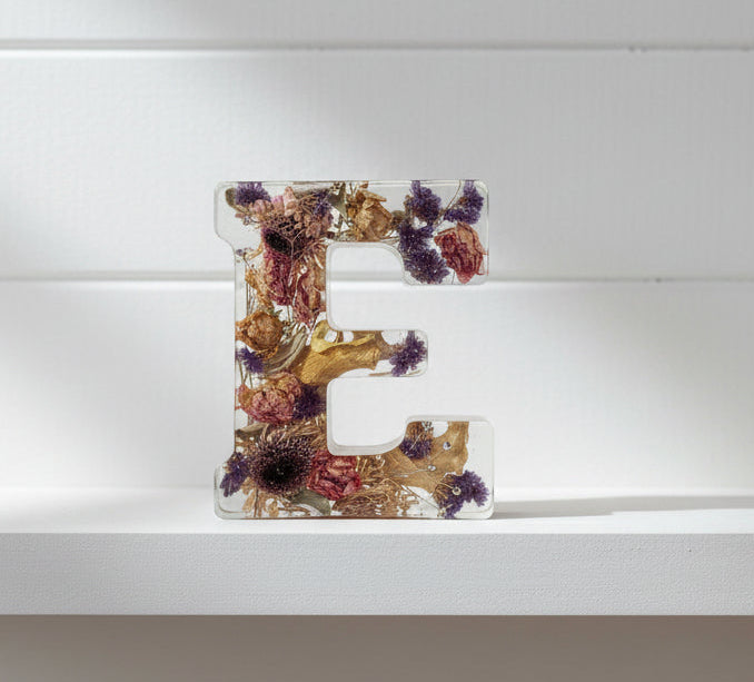 Decorative letters with pressed flowers held by a hand on a white background