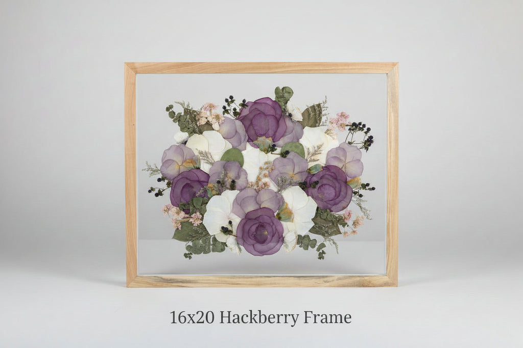 Framed arrangement of pressed flowers with purple and white blossoms on a grey studio
