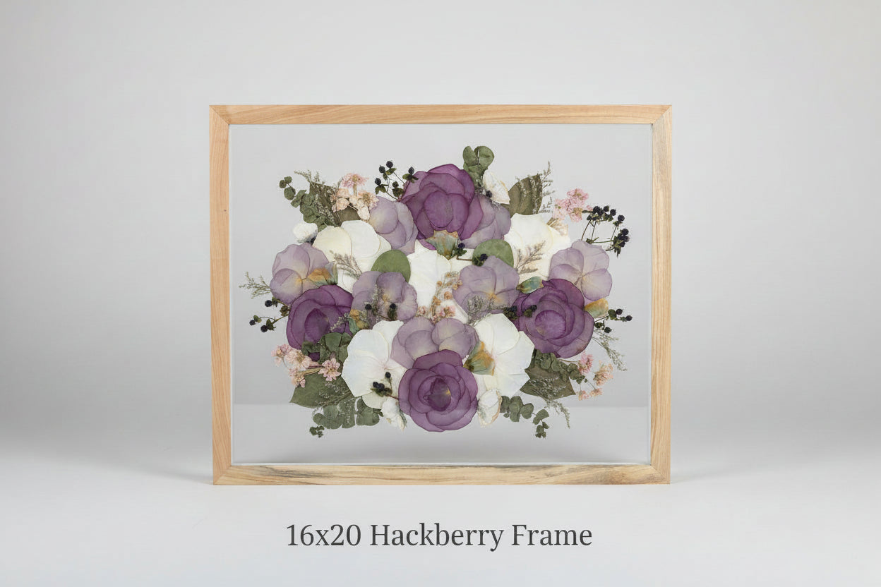 Framed arrangement of pressed flowers with purple and white blossoms on a grey studio