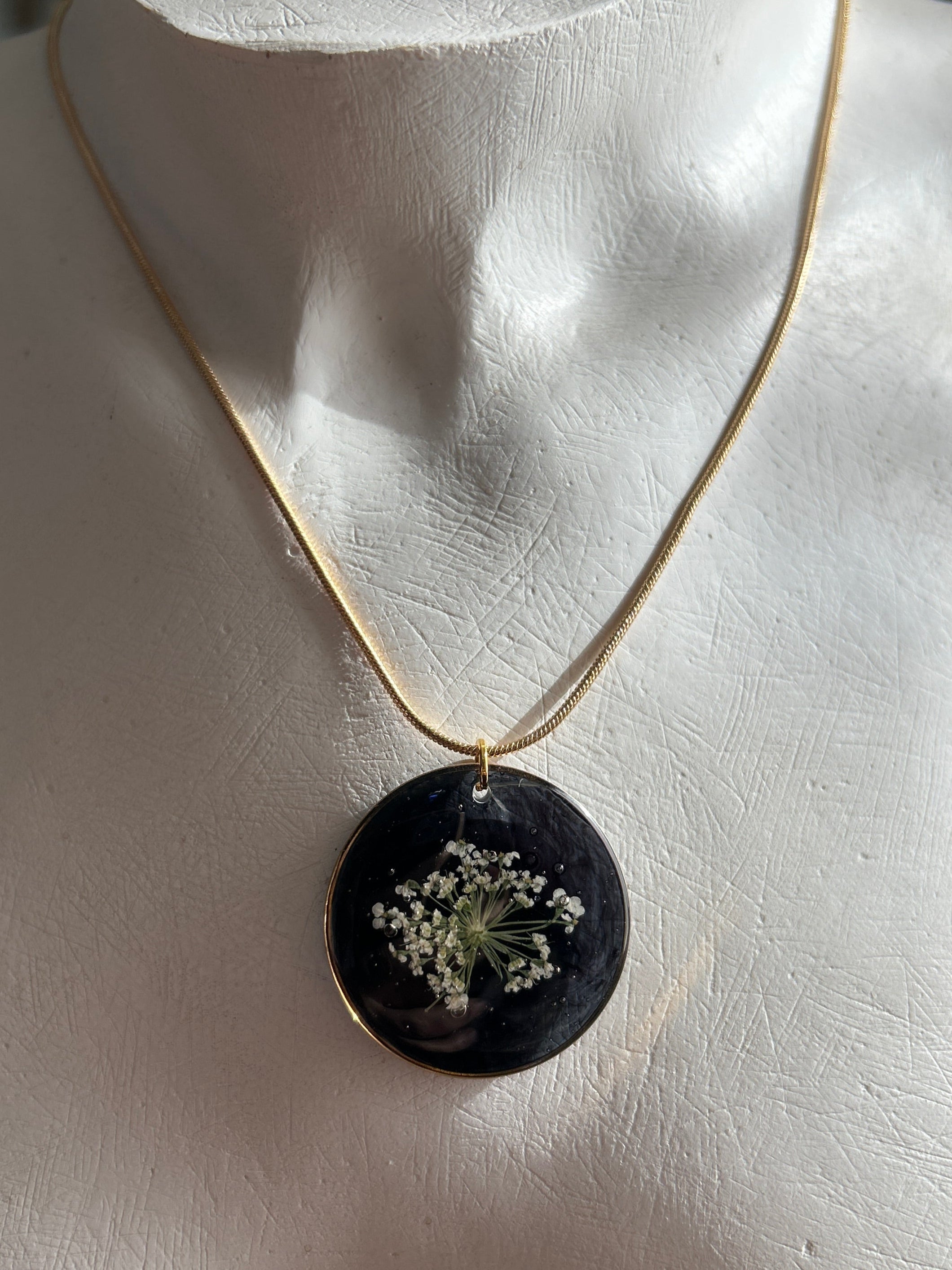 Necklace with a black pendant featuring dried flowers on a mannequin bust.