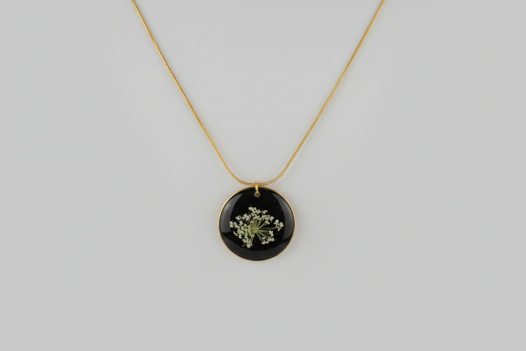 Necklace with a round black pendant featuring a floral design on a light gray background