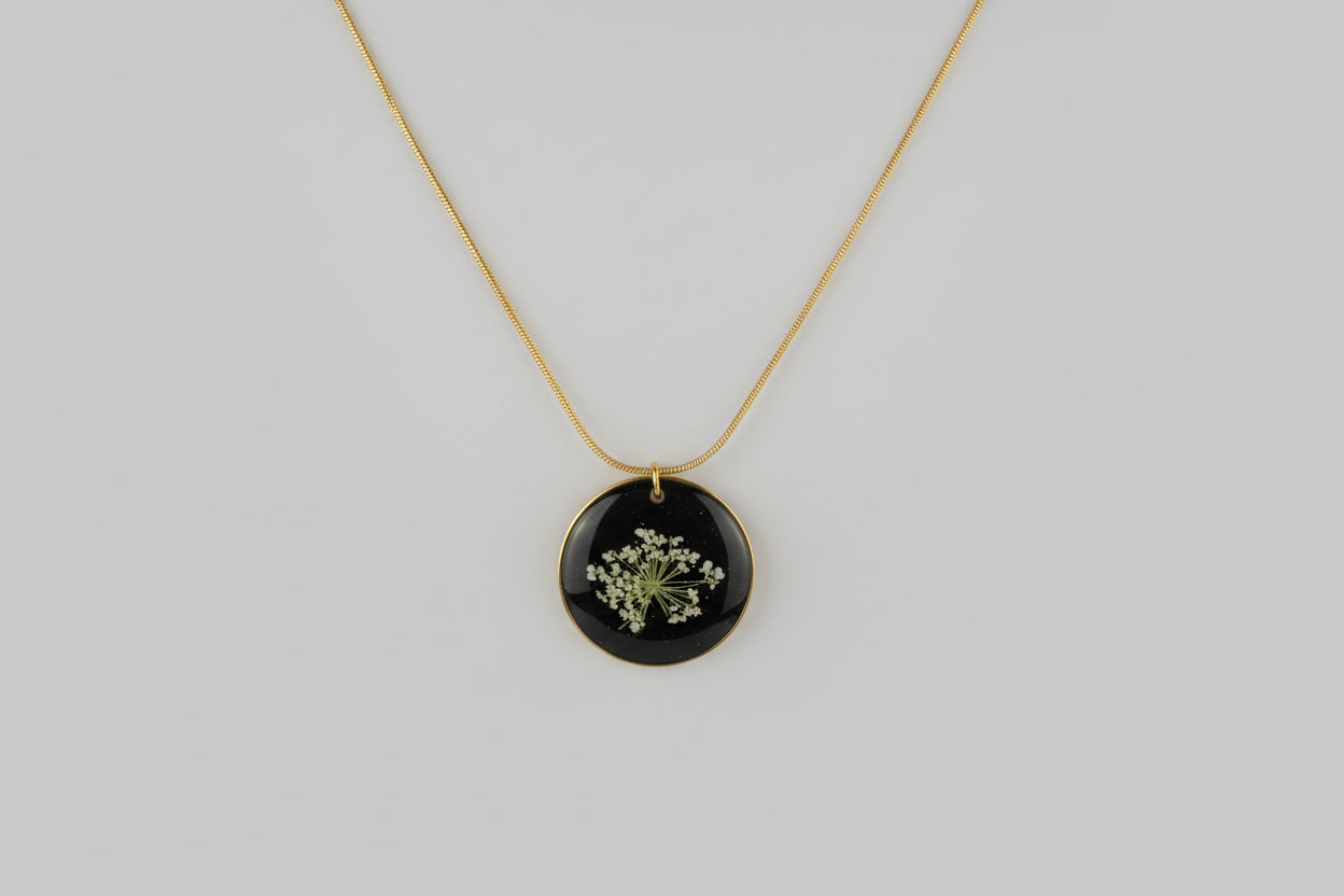 Necklace with a round black pendant featuring a floral design on a light gray background