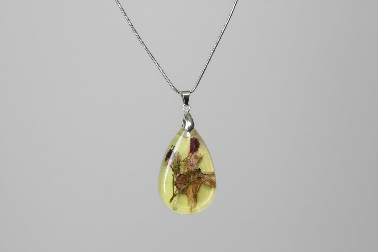 Teardrop-shaped pendant with floral design on a gray background
